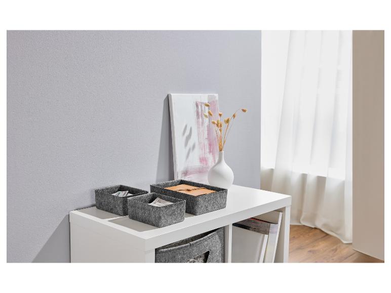 Grijze vilten manden op een witte plank met decoratie.