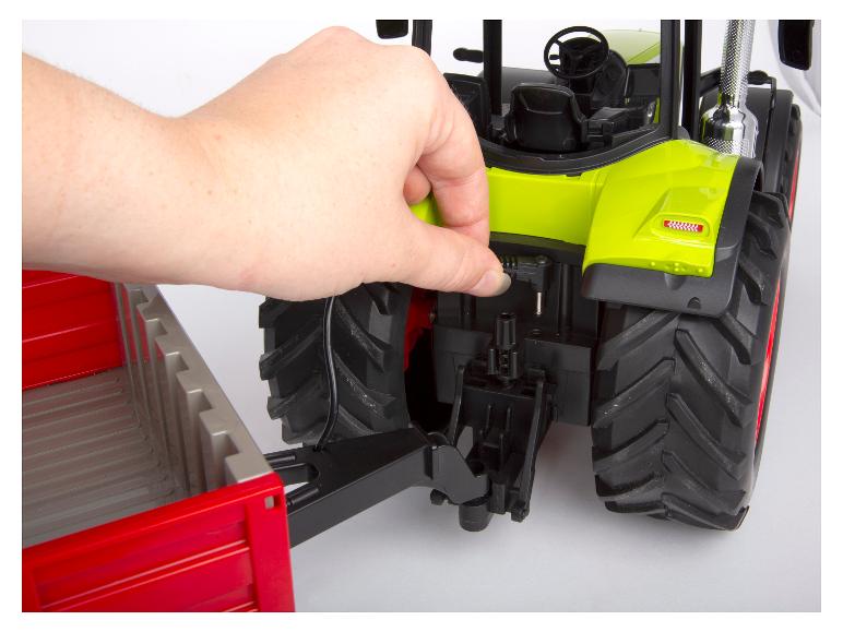 Een aanhanger wordt handmatig aan een Bruder radiografisch bestuurbare tractor gekoppeld.