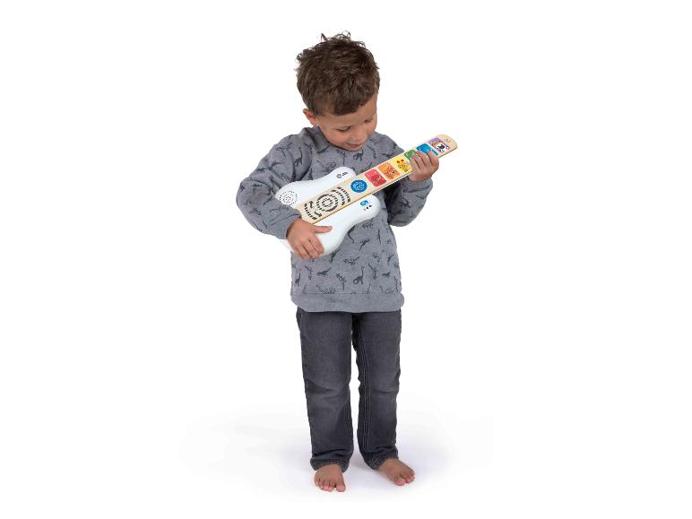 Een jongetje speelt op een witte en houten speelgoedgitaar met kleurrijke knoppen.