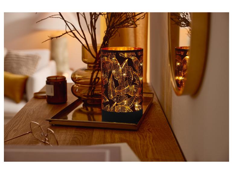 Verlichte tafellamp met bladerenmotief op een houten tafeltje.