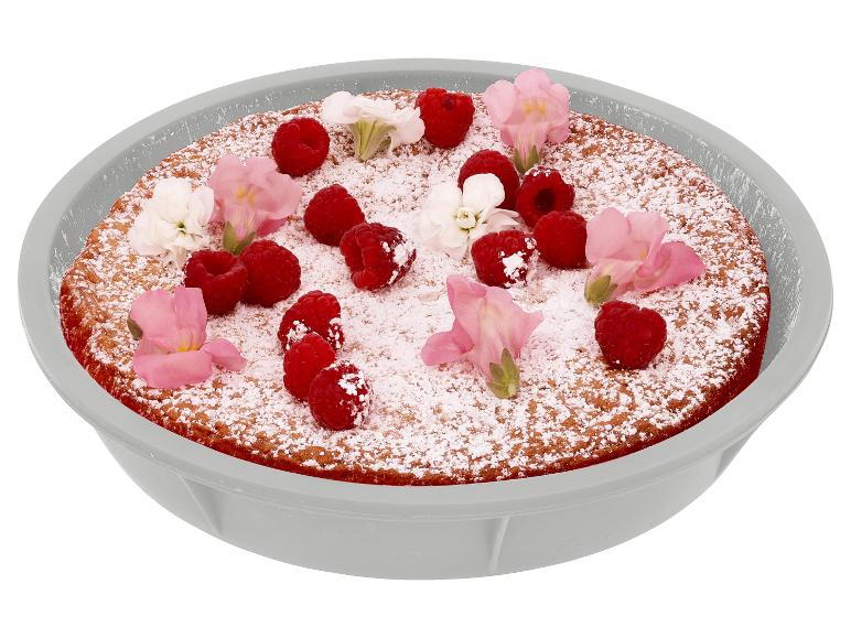Cake met poedersuiker, frambozen en bloemen in een grijze schaal.