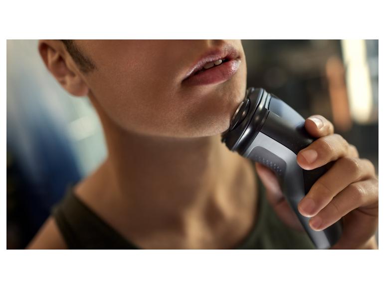 Een man scheert zijn gezicht met een elektrisch scheerapparaat.