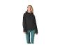 Vrouw in zwarte softshell jas en turquoise broek glimlachend.
