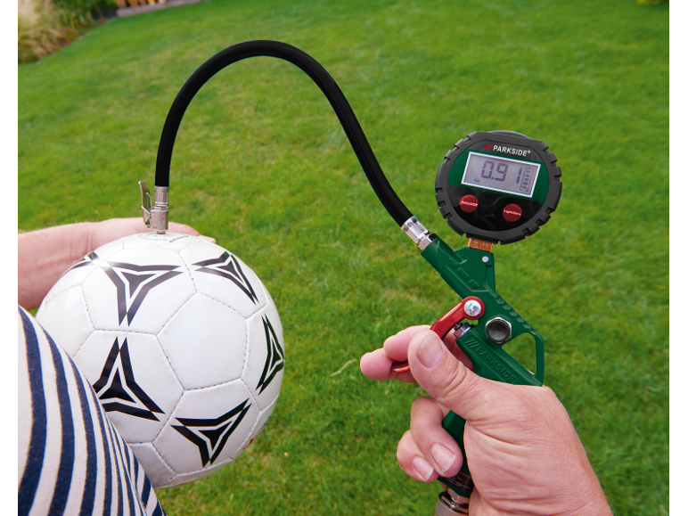 Digitale bandenspanningsmeter die een voetbal oppompt op een grasachtergrond.