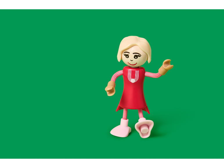 Speelgoedmeisje in een rode jurk met blond haar op een groene achtergrond.