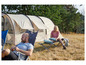 Twee personen relaxen buiten, één in een stoel en de ander op een campingbed, naast een Grand Canyon-tent.