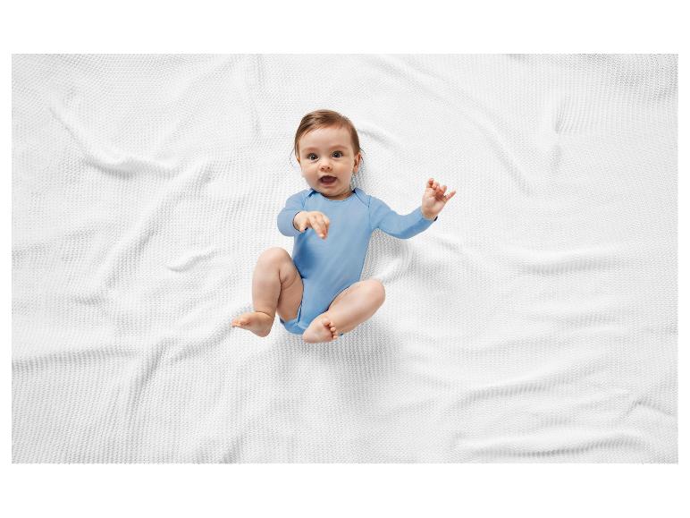 Lachende baby op een witte deken, in een blauw rompertje.