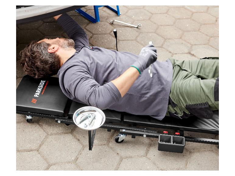 Een monteur ligt op een Parkside Performance werkbank onder een auto.