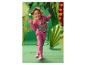 Meisje in roze trainingspak met dinosaurusprint en sneakers, lachend in een papieren jungle-setting.