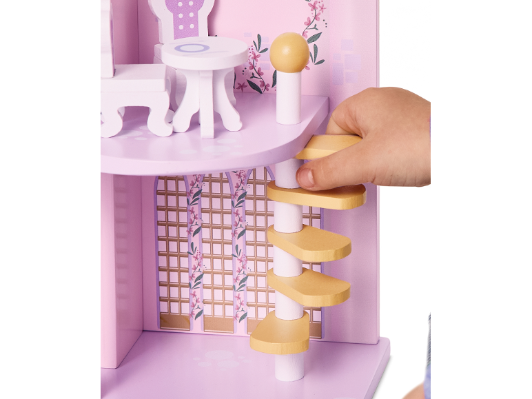 Kinderhand speelt met een roze houten poppenhuis, met meubels en een wenteltrap.
