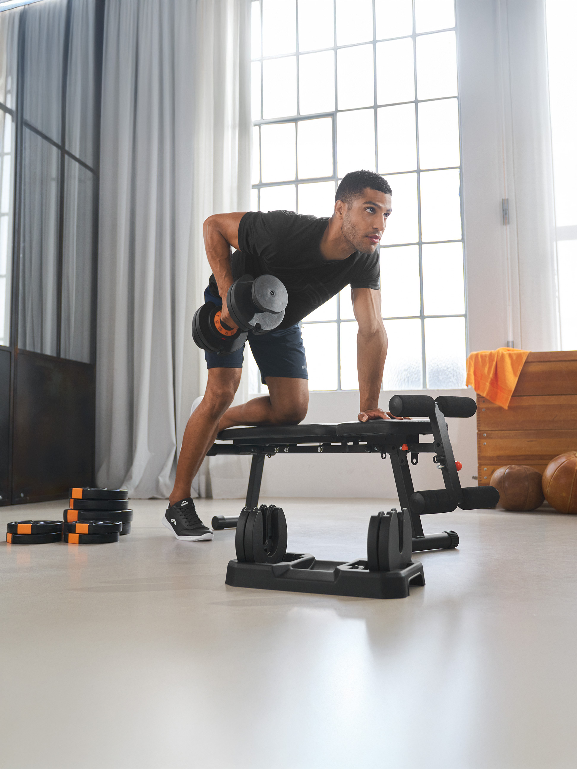 Man traint met verstelbare halter en gewichtsbank in een lichte kamer.