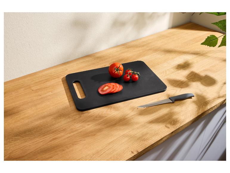 Zwarte snijplank met gesneden en hele tomaten en een mes op een houten aanrecht.