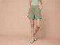 Vrouw draagt groene shorts met bloemenprint en beige sneakers.