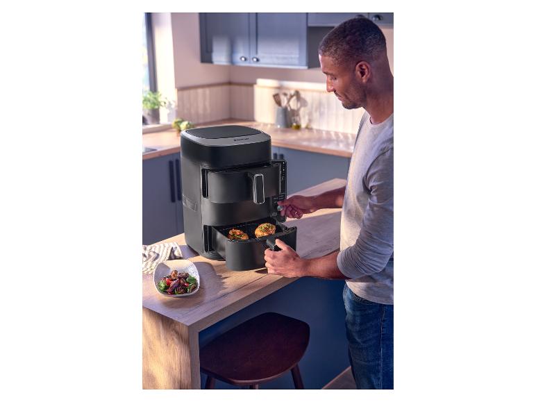 Man gebruikt een zwarte airfryer in de keuken, met een kom salade ernaast.