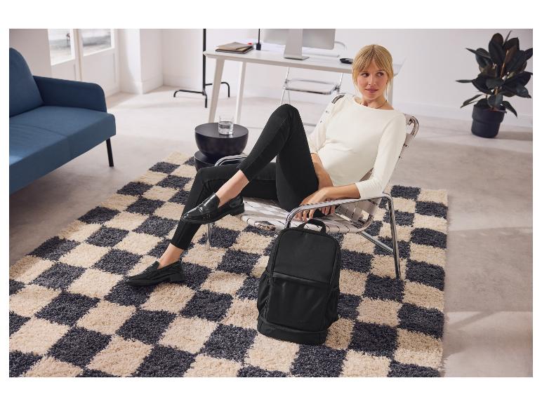 Vrouw in een moderne stoel met een zwarte rugzak naast haar, op een patroonkleed.