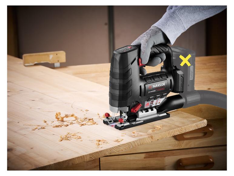 Elektrische decoupeerzaag snijdt een stuk hout, met verspreide houtsnippers.