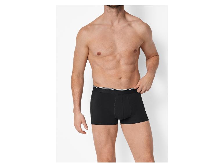 Shirtloze man draagt zwarte boxershorts met een witte tailleband.