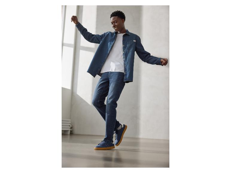 Man in spijkeroverhemd, wit T-shirt, jeans en blauwe sneakers met rubberen zolen.