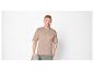 Man in beige T-shirt en groene broek, met een grijze sweater.