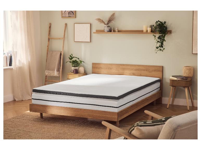 Slaapkamer met houten bed, matras en topper, nachtkastjes en decoraties.