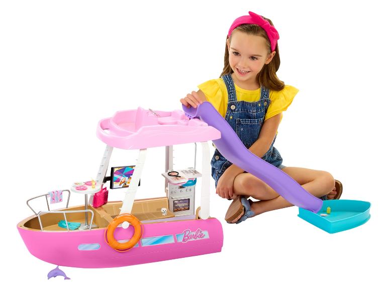 Een lachend meisje speelt met een roze Barbie speelgoedboot, met glijbaan en accessoires.