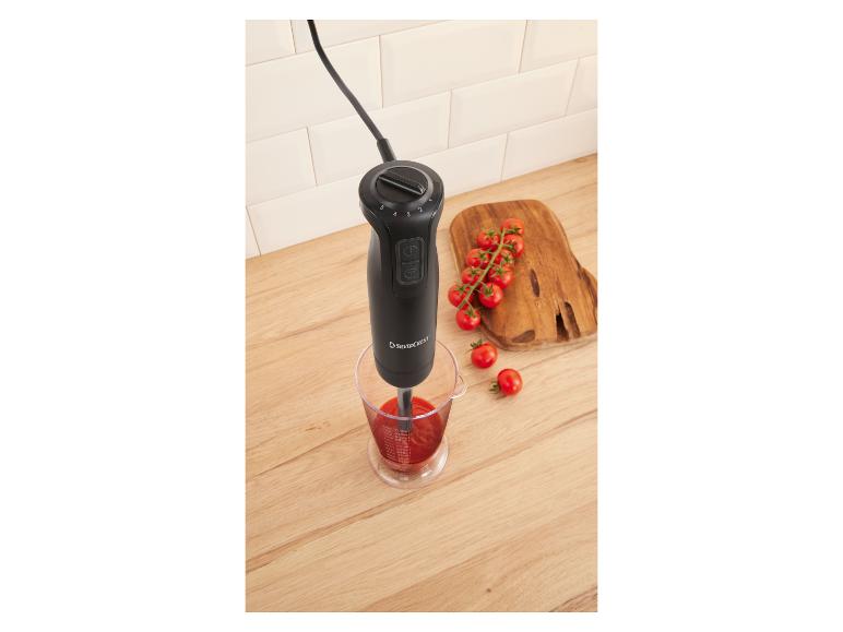 Staafmixer in maatbeker met tomatensaus, cherrytomaten op een houten plank