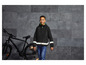 Een jongen draagt een reflecterende zwarte jas met capuchon en staat naast een zwarte fiets.