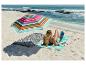 Vrouw leest onder een kleurrijke strandparasol op een gestreepte mat aan zee.