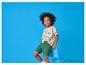 Jongen in dinosaurus T-shirt en groene korte broek, lachend op een blauwe stoel.
