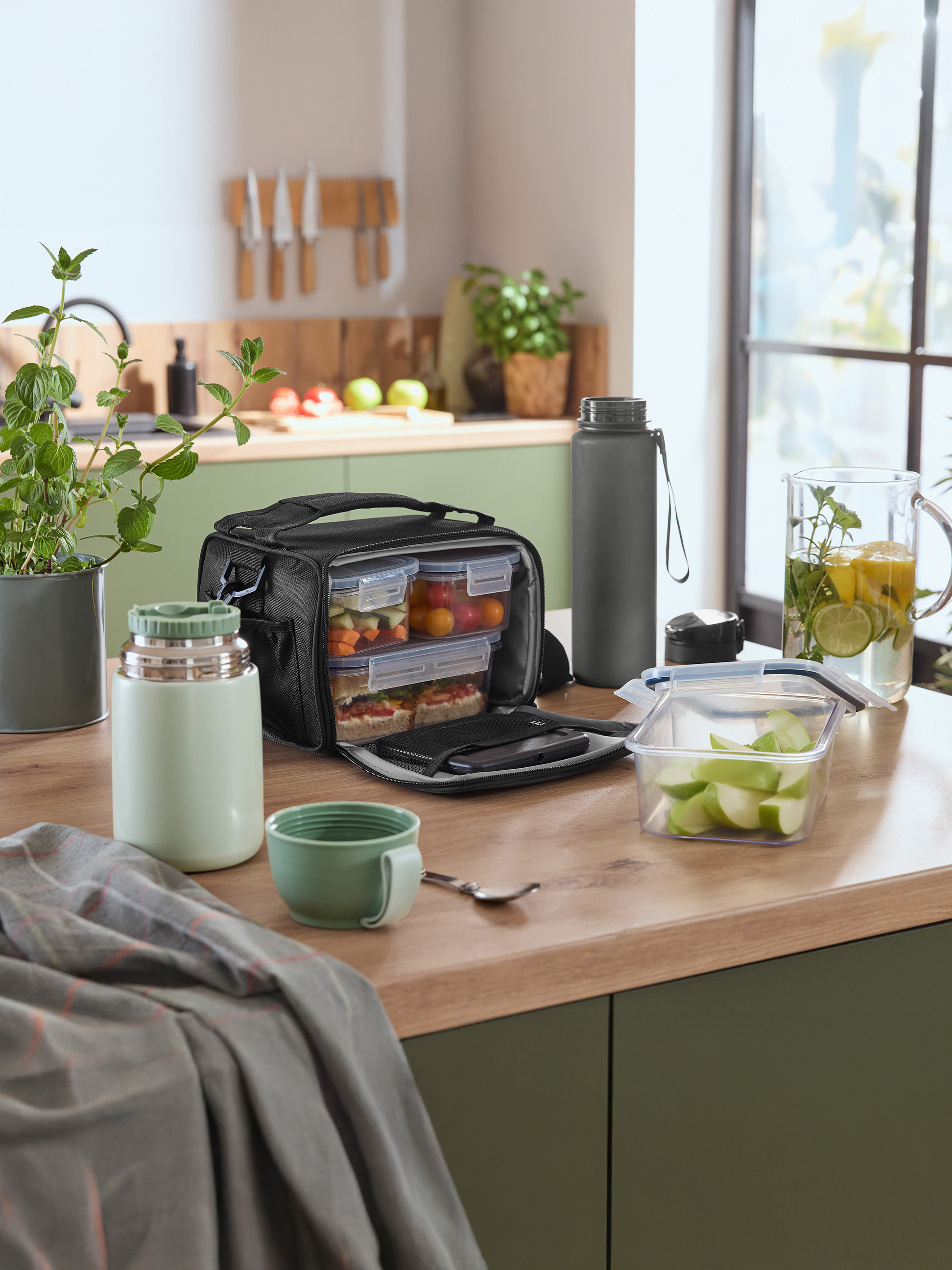 Lunchtas met voedselcontainers, thermosfles en waterfles op een aanrecht.