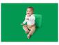 Baby in een wit rompertje met lange mouwen en beige broek, zittend naast een groene kubus.