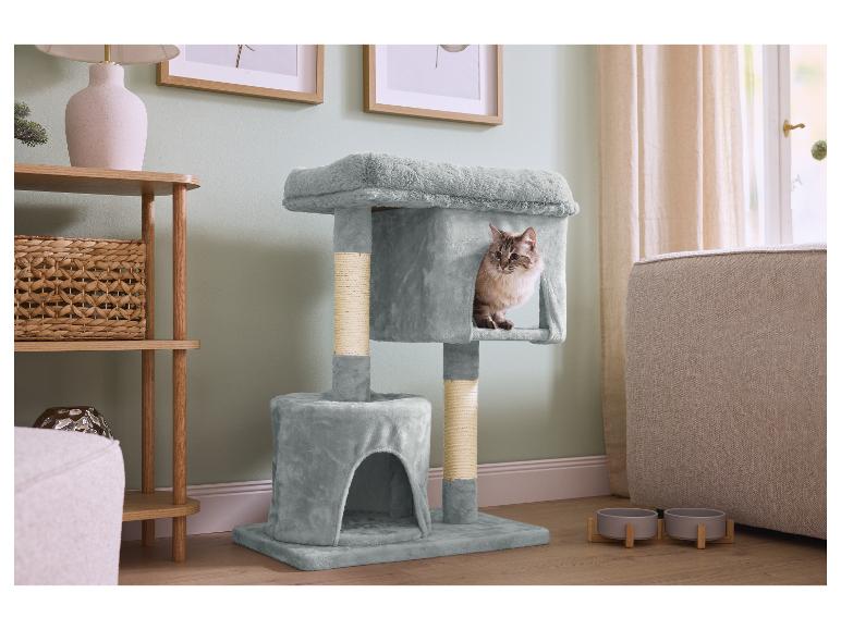 Een kat in een grijze krabpaal, naast een houten plank en voerbakken.