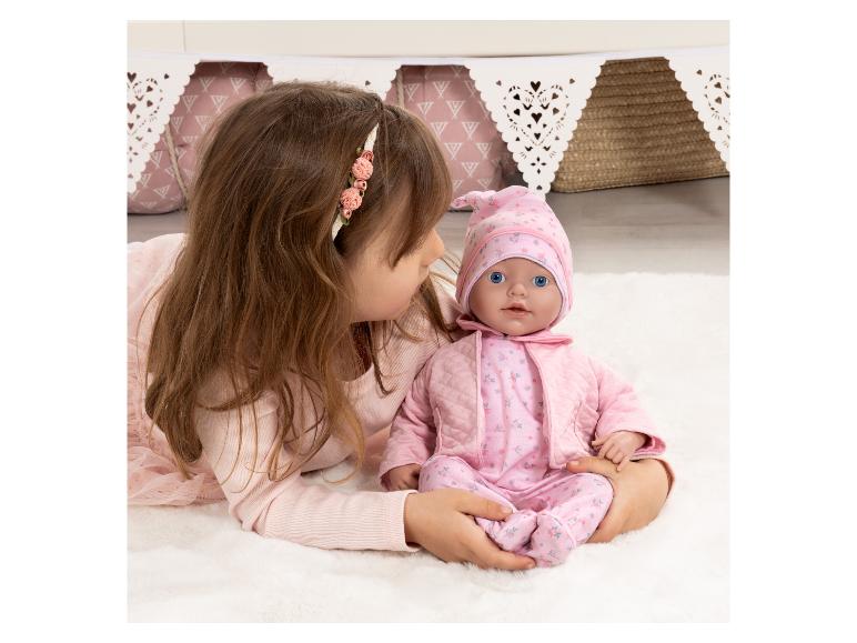 Meisje speelt met een babypop in een roze outfit op een wit kleed.