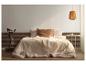 Slaapkamer met bed, licht beddengoed en een geweven hanglamp.