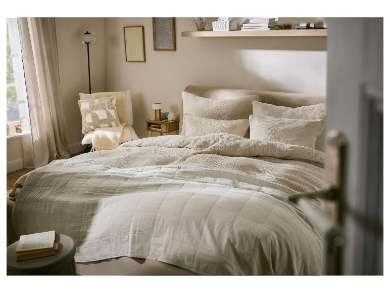 Slaapkamer met bed, beddengoed in linnenlook, sierkussens en een klein bijzettafeltje.