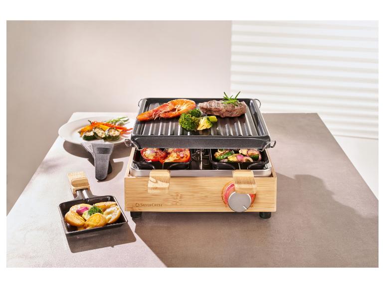 Een bamboe raclette-grill met vlees, garnalen en groenten op de grill en in de pannetjes.