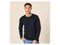 Man draagt een zwart T-shirt met lange mouwen en een blauwe jeans, staand tegen een lichte achtergrond.