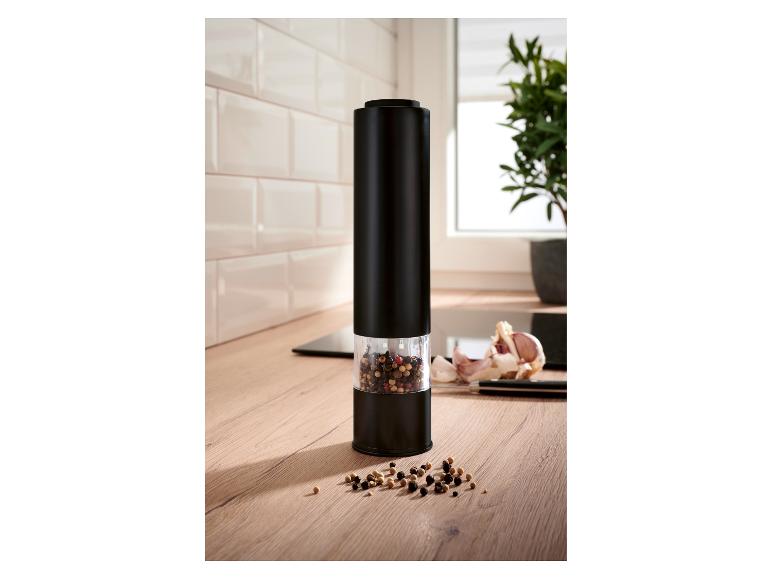 Zwarte elektrische pepermolen met peperkorrels op een houten aanrecht.