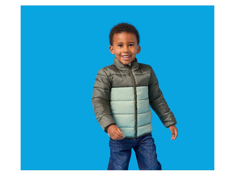 Lachende jongen in een tweekleurige pufferjas en jeans