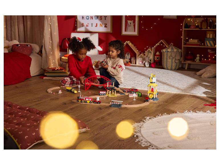 Twee kinderen spelen met een houten speelgoedtrein in een feestelijke kamer.