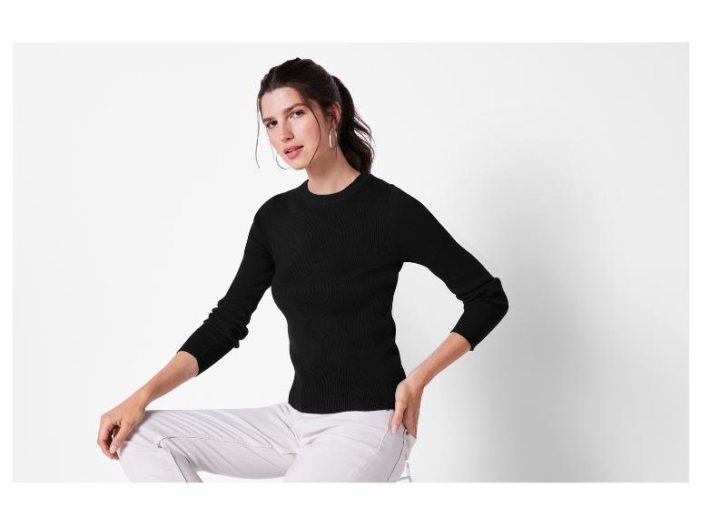 Een vrouw draagt een zwarte trui en witte broek.