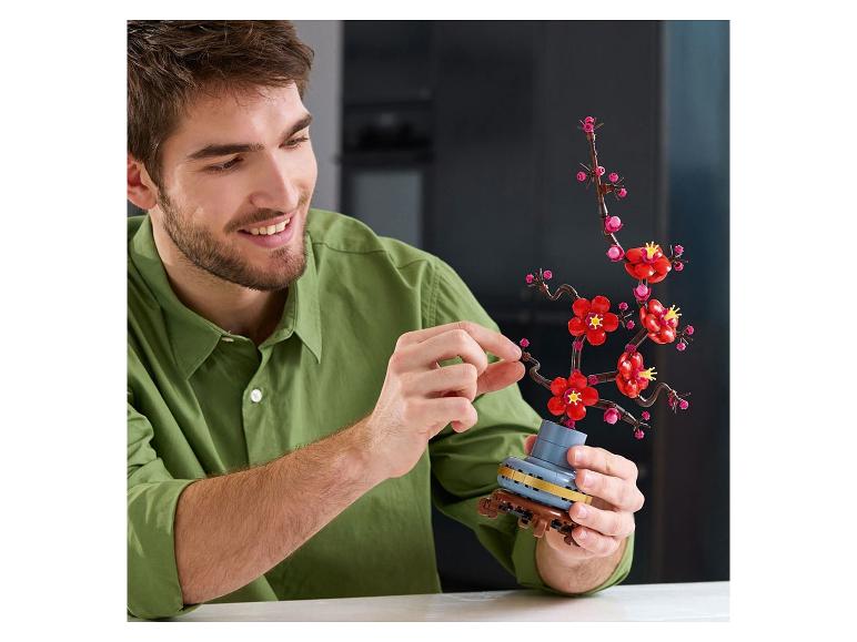 Een lachende man assembleert een kersenbloesem bonsai gemaakt van bouwstenen.