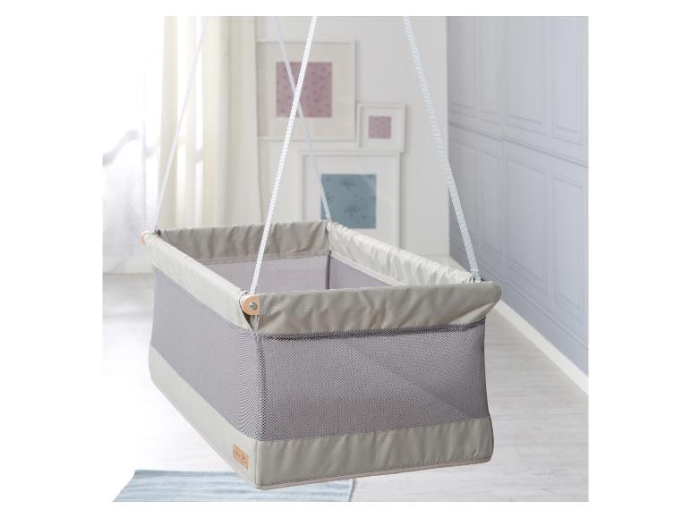 Een grijze en beige hangwieg voor baby's in een lichte kamer.