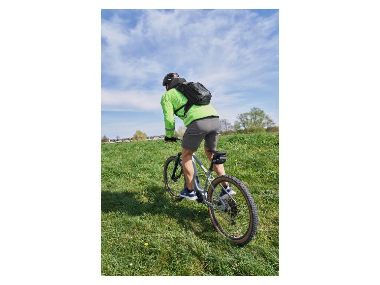 Fietser met rugzak en groen fietsshirt op een mountainbike in een grasveld.