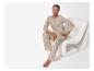 Vrouw in beige pyjama met bloemenpatroon, zittend op een witte stoel.