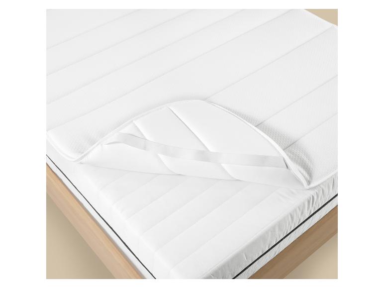 Witte matrasbeschermer met elastische banden op een houten bed.