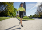 Man in een geel-zwart hardloopjack en zwarte shorts joggend buiten.