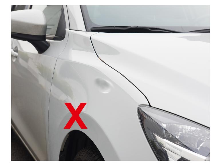 Witte auto met deuk in het spatbord en een rood kruis.