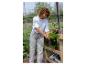 Vrouw in kas met een potkruid, met andere planten en tuinbenodigdheden.