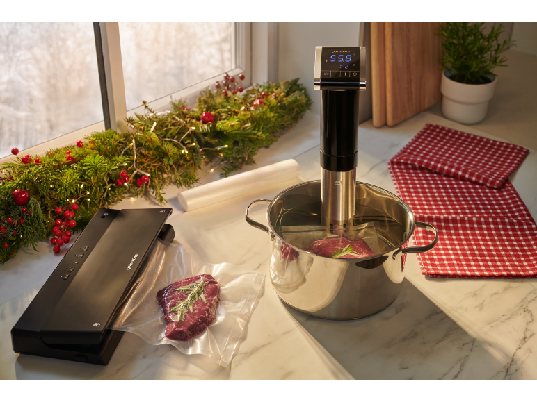Vacumeermachine en sous-vide apparaat met vlees dat kookt in een kerstsfeer.